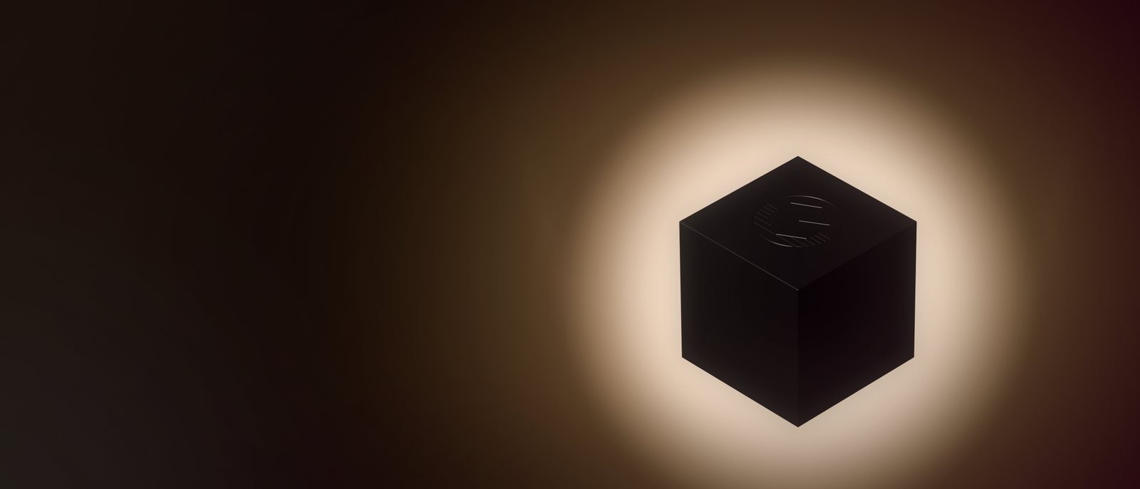 the black cube before the emblem's sun, a soft keylight showing its faces and the emblem on its top