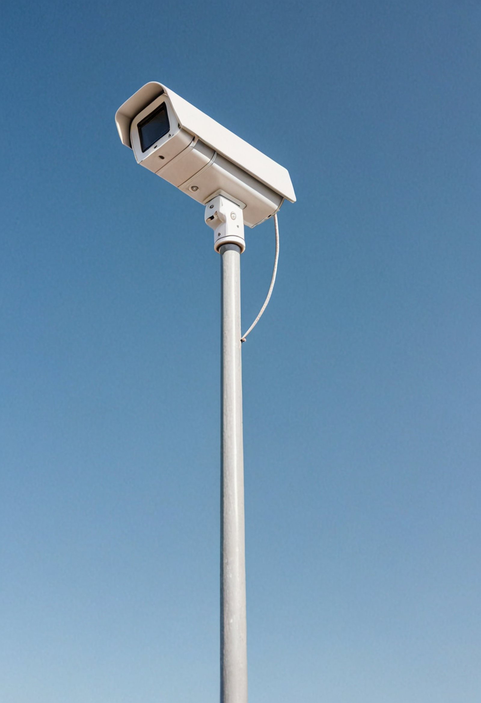 a single white security camera on a tall grey pole